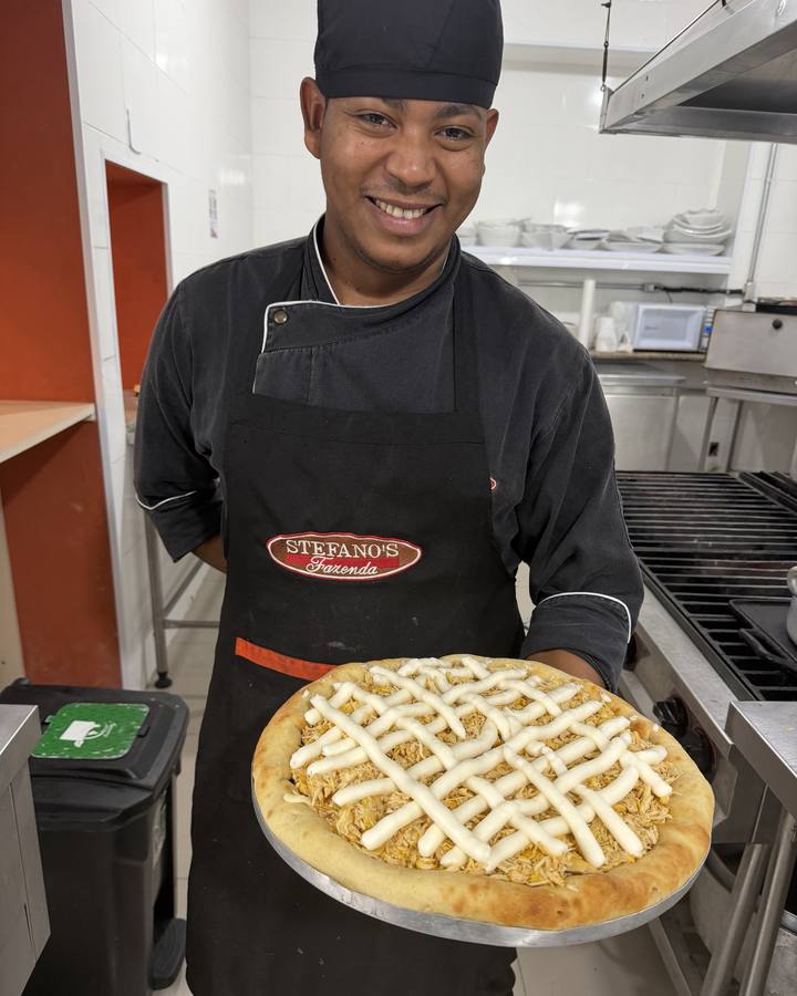 Cozinheiro da casa segurando uma pizza de frango com catupiry